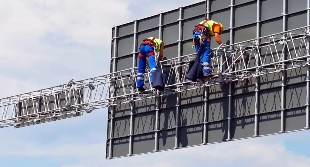Doi lucrători pe structura metalică a unui panou publicitar de mari dimensiuni